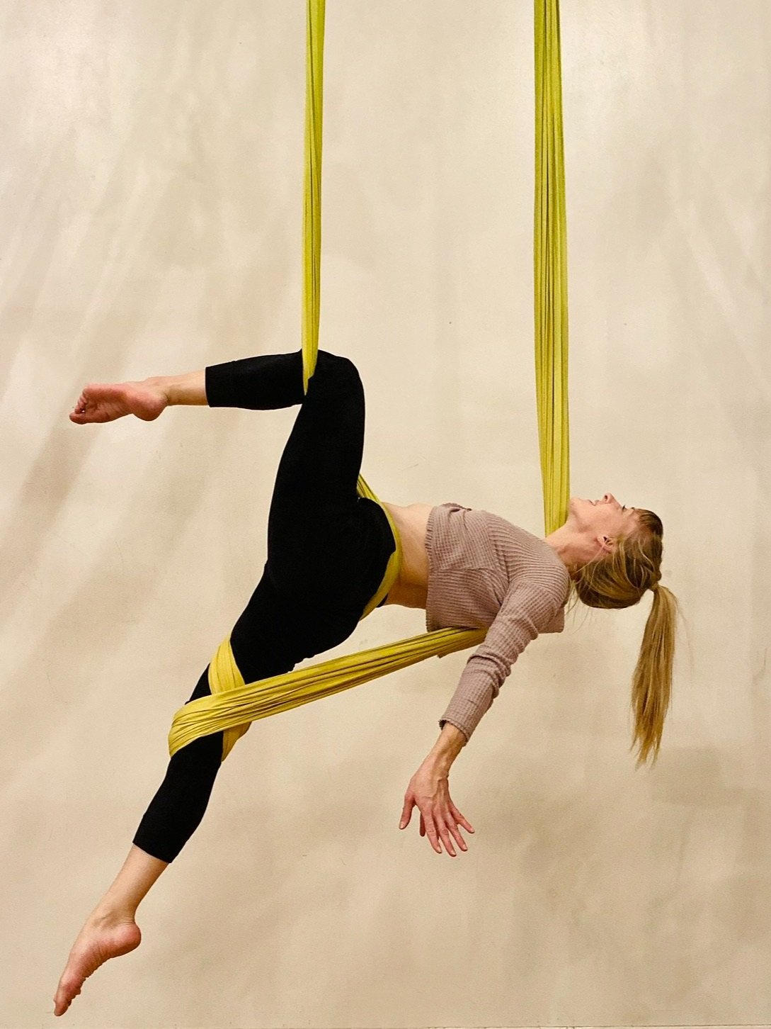 A student suspended in a yellow aerial hammock during an aerial yoga class