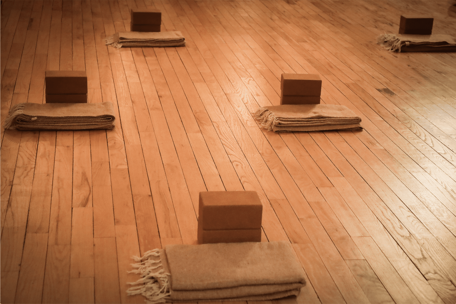 Blankets and cork blocks set out spaced apart on the studio's wood floor before a class