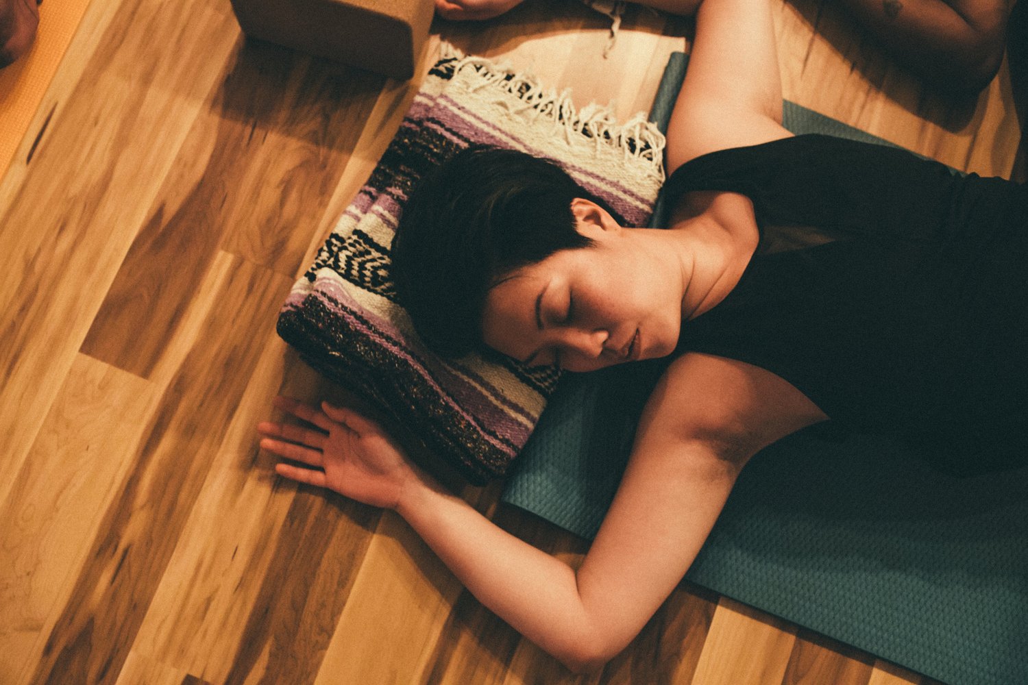 A student resting in savasana on a mat and folded blanket on the studio floor
